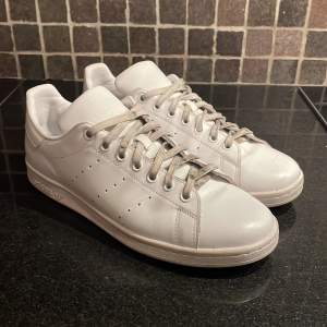 Säljer ett par klassiska vita Adidas Stan Smith sneakers i bra skick. De har en stilren design med snörning och är perfekta för både vardag och fest. Skorna är gjorda i skinn och har en bekväm passform. Skorna är i stort sätt helt nya. Storlek 42. Snörena är lite smutsika då det kommer från ett annat par Stan Smiths då snörena till dessa gick sönder i en rulltrappa😁 hör av digvid minsta lilla fråga🫵🫵🫶