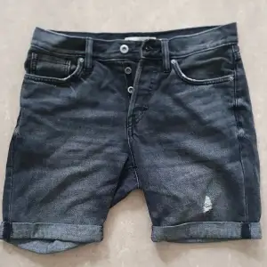 Snygga svarta jeansshorts från H&M i bra skick. De har en klassisk femficksdesign och är lågmidjade med knappgylf. Perfekta för sommardagar eller en avslappnad stil. De har en liten slitsdetalj på framsidan för en cool look.