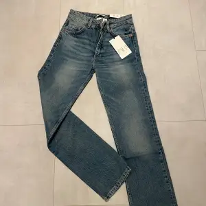 Säljer ett par snygga blå jeans från Zara i straight fit och ankel-längd. De är i nytt skick med prislapp kvar och har en klassisk femficksdesign med knapp och dragkedja framtill. Perfekta för både vardag och fest! Skulle säga att dessa är små i modellen