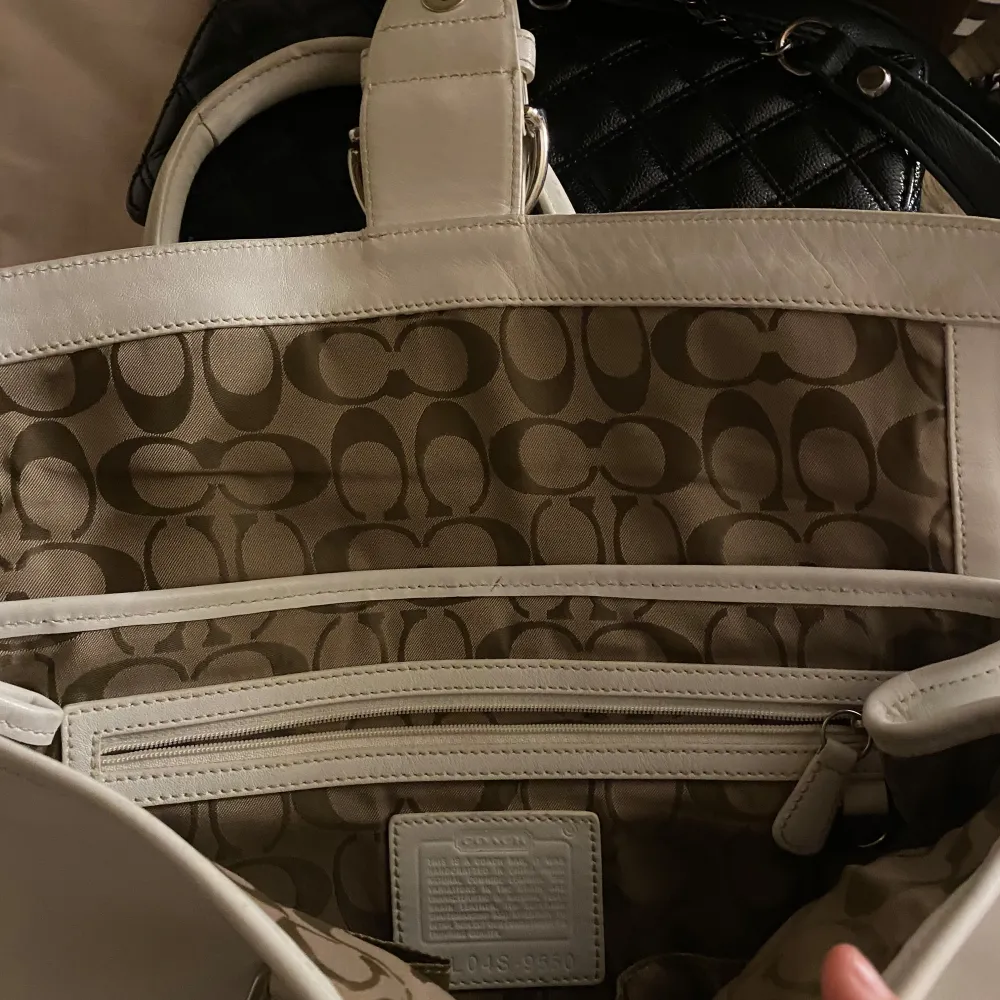 Säljer en elegant vit handväska från Coach i skinn. Väskan har en stilren design med ett dekorativt bälte och en praktisk dragkedja inuti. Perfekt för både vardag och fest! 👜✨. Väskor.