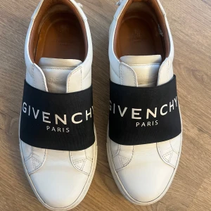Vita sneakers från Givenchy - Säljer ett par stilrena vita sneakers från Givenchy i bra skick. Skorna är tillverkade i skinn och har en klassisk design med rund tå och låg profil. Perfekta för både vardag och fest! Använt ett fåtal gånger, säljer pga nya skor. Upplever dem som lite stora i storleken, har vanligtvis 38 men dessa sitter perfekt. Köpta i Milano. Skokartongen, dustbag och kvitto medföljer! Har även påsen kvar om så önskas. Nypris ligger runt 6000:- 