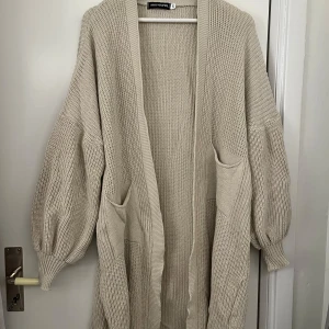 Beige stickad kofta från Missy Empire - Supermysig beige stickad kofta från Missy Empire. Perfekt för kyliga dagar med sina långa ärmar och stora fickor. Den har en loose passform som gör den extra bekväm att bära över vilken outfit som helst. Ett måste för höst- och vintergarderoben!