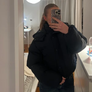 Mörkblå pufferjacka - Säljer en mörkblå pufferjacka i mycket bra skick. Den är perfekt för kalla vinterdagar och har en skön, oversized passform. Jackan har långa ärmar och stängs med dragkedja och knappar. Supermysig och varm!