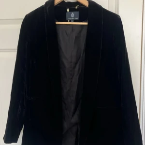 Svart kavaj från Stockh LM - Snygg svart kavaj från Stockh LM i storlek 36. Perfekt för både fest och vardag med sin eleganta design. Kavajen har långa ärmar och en klassisk passform. Materialet känns lyxigt och ger en stilren look. Passar utmärkt till höst och vinter, även sommar och vår kvällar.