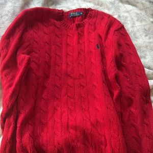 Röd stickad tröja från Polo Ralph Lauren - Säljer en snygg röd stickad tröja från Polo Ralph Lauren med kabelstickat mönster. Tröjan har långa ärmar och en klassisk rund halsringning. Perfekt för kyligare dagar!  Fraktar samma dag! Pris diskuteras gärna 