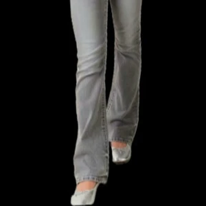 Grå bootcut jeans - Snygga grå bootcut jeans med klassisk femficksdesign och knappdetaljer. Perfekta för en avslappnad stil med en touch av retro. Passar bra till både sneakers och klackar.