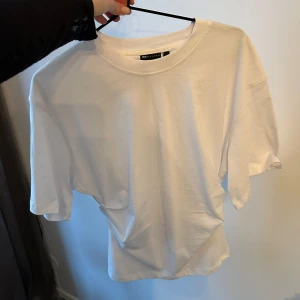 Vit t-shirt med indragen midja  från ASOS DESIGN - Säljer en vit t-shirt från ASOS DESIGN med indragen midja. Ger väldigt fin siluett. Perfekt basplagg för alla tillfällen.