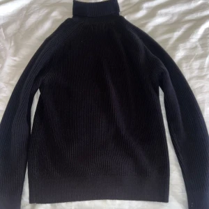 Mörkblå stickad East west tröja - Säljer en stilren mörkblå stickad east west tröja i storlek M. Perfekt för kyligare dagar med sin höga krage och ribbade struktur. Passar både till vardags och mer uppklädda tillfällen.