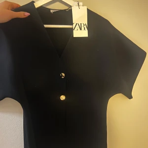 Svart tröja från Zara - Elegant svart topp från Zara med kortärmad design och stilrena knappar framtill. 