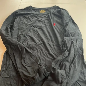 Svart långärmad tröja från Polo Ralph Lauren - Säljer en svart långärmad tröja från Polo Ralph Lauren med det klassiska röda logotypbroderiet på bröstet. Perfekt för en stilren och avslappnad look. Tröjan är tillverkad i mjukt material för extra komfort.