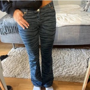 Blå zebra-mönstrade bootcut jeans - Snygga blå jeans med zebra-mönster och bootcut-stil. De har en klassisk femficksdesign och knappar i guldton. Perfekta för att sticka ut med en unik look.