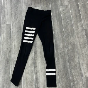 Svarta leggings med vita ränder från H&M - Snygga svarta leggings från H&M med vita ränder på ena benet. Perfekta för en sportig look eller avslappnad stil. Tillverkade i ett stretchigt material för bästa komfort.
