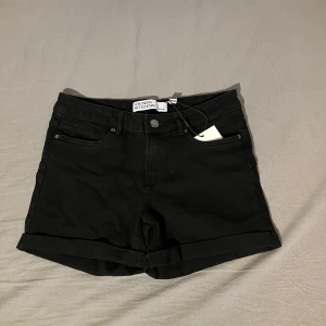 Svarta jeansshorts från Vero Moda VMLuna  - Aldrig använda. Snygga svarta jeansshorts från Vero Moda med uppvikta ben och klassisk femficksdesign. Perfekta för en stilren look. De har en knapp och dragkedja framtill för enkel stängning.