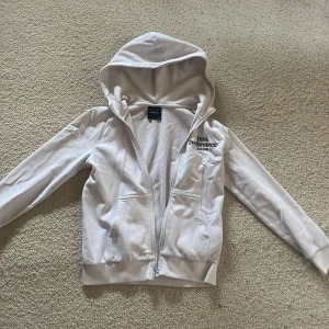 Vit hoodie från Peak Performance - Säljer en snygg vit hoodie från Peak Performance med dragkedja och huva. Insidan är fodrad med mjuk fleece för extra komfort. Perfekt för kyliga dagar. Den har långa ärmar och ribbade muddar vid ärmslut och nederkant.