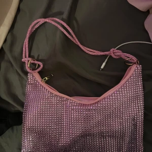 Rosa glittrig axelväska - Snygg rosa axelväska med glittrande paljetter och dragkedja. Perfekt för att ge en extra touch till din outfit. Väskan har en enkel design med dubbla axelremmar.