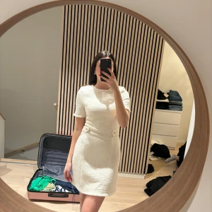 Vit kortklänning med knappar - Twedad - Snygg vit kortklänning med rund hals och korta ärmar. Klänningen har dekorativa knappar i midjan som ger en elegant touch. Perfekt för en stilren look.