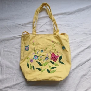 Gul shoppingväska med broderade blommor - Charmig gul shoppingväska med broderade blommor och fjärilar i olika färger. 