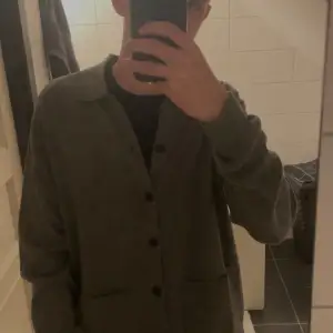 Säljer en stilren grå kofta från Massimo Dutti i 100% ull. Koftan har långa ärmar och knappar framtill, perfekt för kyligare dagar. Den är mjuk och bekväm, vilket gör den till ett utmärkt val för både vardag och mer uppklädda tillfällen.