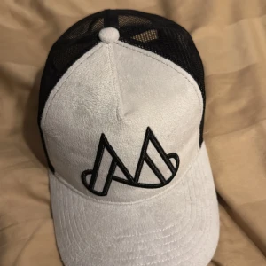 Vit och svart keps med broderad logga - Snygg vit keps med svart broderad logga framtill. Kepsen har en svart mesh-bakdel för extra ventilation och justerbar passform. Perfekt för en avslappnad stil.