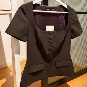 Mörkbrun topp Zara - Så snygg mörkbrun kostymtopp från Zara med knappar och två dekorativa fickor! Färgen är mörkare i verkligheten!!! Aldrig använd, har lappen kvar!! Säljer denna då den inte passade mig. Storlek M men passar även S 🩷🩷 Nypris är 400kr!