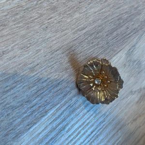 Guldfärgad blomformad ring - Elegant guldfärgad ring i form av en blomma med detaljerade kronblad och en glittrande sten i mitten. Perfekt för att ge en touch av glamour till din stil.