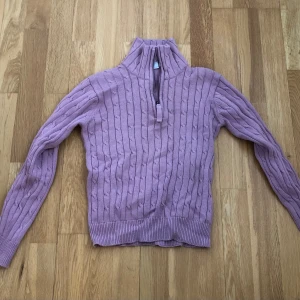 Ljuslila stickad tröja från Isolde - Säljer en ljuslila stickad tröja från Isolde med kabelstickat mönster och dragkedja vid halsen. Tröjan har långa ärmar och en hög krage som ger extra värme. Perfekt för kyliga dagar! Den är lite i storleken, kort i ärmarna för mig som brukar ha storlek S.