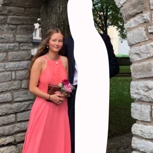 Korallfärgad långklänning från JJ's House - Elegant korallfärgad långklänning från JJ's House med spetsdetaljer på överdelen. Klänningen har smala axelband och en flytande kjol som ger en vacker silhuett. Perfekt som exempelvis balklänning. Finns inga defekter och den passar mig som har storlek M på allt💕