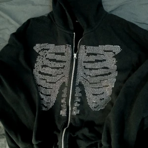 Zip up med kristaller ☆ - Säljer en zipup hoodie med kristaller och skelett tryck!!! Storleken är M men jag har storlek L och den sitter fortfarande baggy på mig :3 dock har några kristaller kommit av vilket ni kan se på bilden! pris kan diskuteras <3 