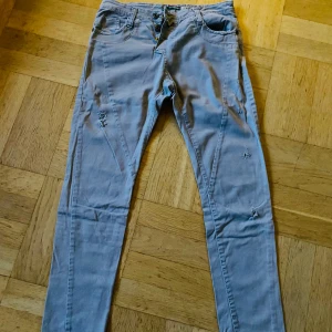 Grå/beiga byxor från Please - Snygga ljusa byxor från Please med slitna detaljer och knappgylf. Byxorna har en hjärtformad detalj på bakfickan och är perfekta för en avslappnad stil. De har en normal passform och är tillverkade i ett bekvämt material. 