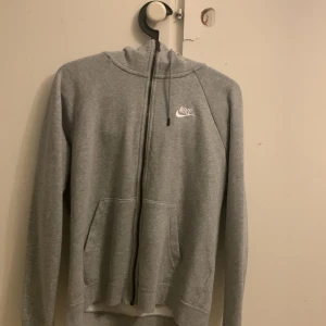 Grå hoodie från Nike - Säljer en klassisk grå hoodie från Nike med dragkedja och huva. Tröjan har långa ärmar och en praktisk ficka framtill. Perfekt för en avslappnad stil.
