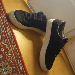 Svarta sneakers med vit sula - Snygga svarta sneakers med vit sula och snörning. Perfekta för en avslappnad stil. Skorna har en klassisk design med rund tå och är tillverkade i ett material som ser ut som mocka.