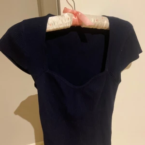 Mörkblå ribbad topp från Gina Tricot - Säljer en snygg mörkblå ribbad topp från Gina Tricot. Toppen har en elegant passform med korta ärmar och en v-ringad hals. Perfekt för en stilren look.