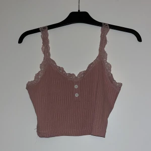 Rosa ribbad linnetopp med spetsdetaljer - Rosa ribbat linne med spetsdetaljer och knappar. 🩷