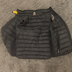 Svart dunväst från Parajumper.perfekt- down vest.  - Säljer en snygg svart dunväst från Parajumpers. Västen har en dragkedja framtill och två praktiska fickor med dragkedjor. Insidan är ljusgrå och den har en hög krage för extra värme. Perfekt för lager-på-lager under kyliga dagar och även varma dagar där man kan bära den med bara en T-shirt under. Super bra skick, nästan aldrig använd och inga hål eller något. Utspungs pris: 3899. Det är smal och är 70 cm fårn axlarna och ner