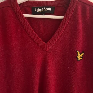 Röd tröja från Lyle & Scott - Snygg röd tröja från Lyle & Scott med v-ringning och deras logga på bröstet. Perfekt för en stilren look.