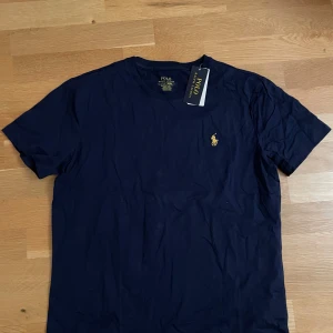 Mörkblå t-shirt från Polo Ralph Lauren - Säljer en stilren mörkblå t-shirt från Polo Ralph Lauren med det klassiska broderade logotypen i gult på bröstet. Perfekt för en avslappnad look. Kortärmad och i mjukt material.