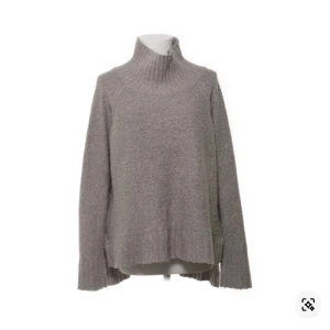 Grå stickad polotröja - Säljer en mysig grå stickad polotröja med hög krage. Tröjan har långa ärmar och en lös passform, perfekt för kyliga dagar. Den ribbade strukturen ger en stilren look. Passar utmärkt till både jeans och kjol.