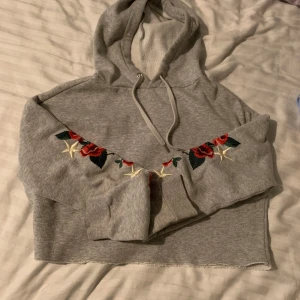Grå crop topp hoddie från H&M  - Säljer en grå crop topp hoodie från H&M med röda rosor på armarna,Perfekt för en avslappnad stil!