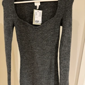 Grå klänning oanvänd  - Säljer en stilren grå klänning med lång ärm och djup v-ringning. Perfekt för kyligare dagar och enkel att matcha med olika outfits. 