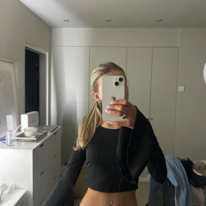 Svart croppad långärmad topp - Snygg svart croppad topp med långa ärmar och utsvängda ärmslut. Perfekt för en trendig look.