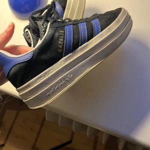 Adidas Gazelle högsula - Adidas Gazelle sneakers i svart och lila/blå i mocka. Hög sula, storlek 38 1/3. Använda men bra skick. 