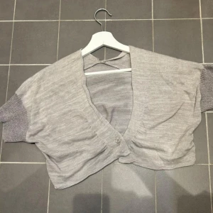 Grå bolero - Säljer en stilren grå bolerotopp med korta ärmar och knappar framtill.  Super fin till ett linne och bra till våren! Skick 9/10💯