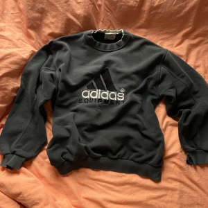 Svart sweatshirt från Adidas - Säljer en svart sweatshirt från Adidas med deras klassiska logga broderad på framsidan. Tröjan har långa ärmar och en rund halsringning. Perfekt för en avslappnad stil.