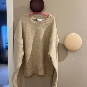 Beige tröja från Zara - Säljer en stilren beige tröja från Zara. Den har en rund halsringning och långa ärmar med ribbade kanter. Perfekt för en avslappnad och trendig look. Aldrig använd bara testad men prislappen är inte kvar.