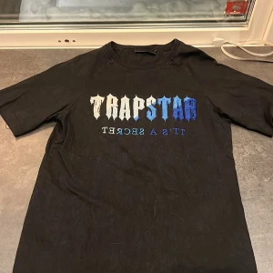 Svart t-shirt från Trapstar - Snygg svart t-shirt från Trapstar med tryck i vitt och blått på framsidan. Perfekt för en casual look. Kortärmad och i normal passform.