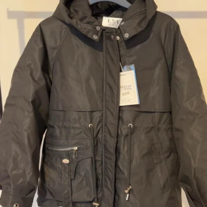 Svart vinterjacka från Lixueyao - Snygg svart vinterjacka från Lixueyao med dragkedja och knappar. Jackan har en mysig fuskpälsfoder på insidan och praktiska fickor med dragkedja. Perfekt för kyliga dagar med sin justerbara midja och huva.