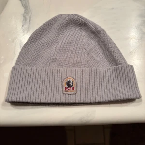 Grå ribbad mössa från Parajumpers - Snygg grå ribbad mössa från Parajumpers med broderad logga framtill. Perfekt för kyliga dagar med stilren design och mjukt material. Har aldrig använt så skick är 10/10. 
