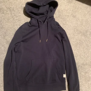 Mörkblå hoodie - Säljer en stilren mörkblå hoodie med känguruficka och justerbar huva. Perfekt för en avslappnad look. Den har långa ärmar och en mjuk känsla från märket Jack and Jones. Storlek: S.