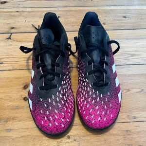 Adidas Predator fotbollsskor - Snygga Adidas Predator fotbollsskor i svart och rosa med vita detaljer. Skorna har en unik mönstrad ovandel och snörning för optimal passform. Perfekta för spel på konstgräs.