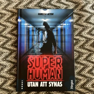 Bok Super Human: Utan att synas - Spännande bok av Vanessa Acton, 'Super Human: Utan att synas', utgiven av Hegas. Omslaget visar en mystisk figur i en korridor med blå skåp och en lysande titel i rött. Perfekt för den som gillar action och mysterier.